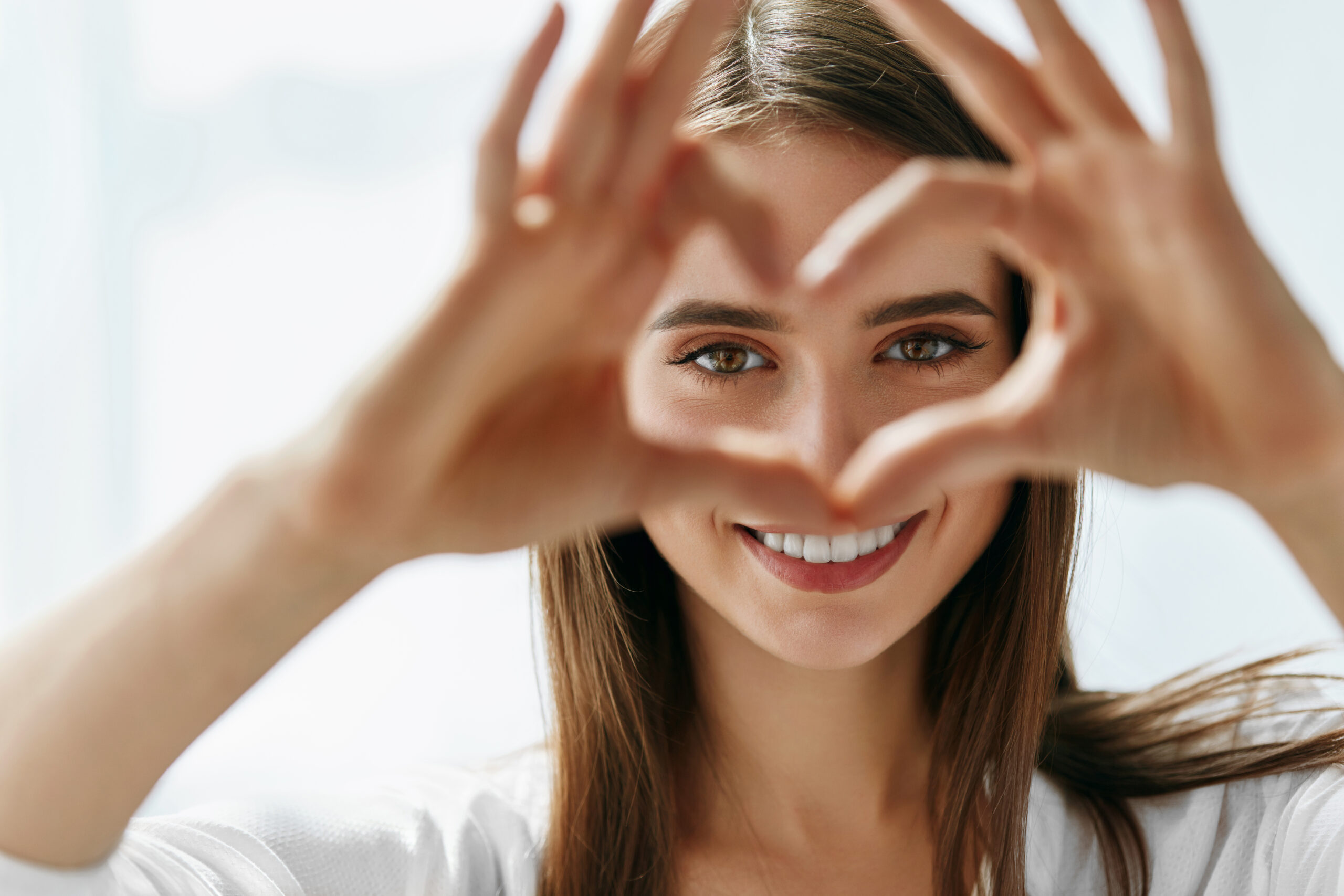 Head shot image of a pretty woman making a heart shape with her hands with her eyes showing through